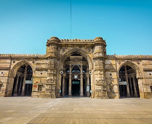 Three-arch stone gateway under a bright blue sky; a central grand arch flanked by two smaller arches, opening into a courtyard.