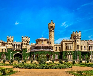 Castle-like historic building with multiple towers and a central tall tower, set in a manicured courtyard with hedges under a blue sky.