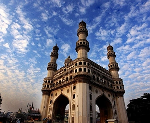 Historic gateway with arches and four minarets, set against a bright blue sky.