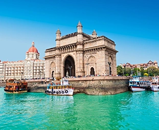 Gateway of India monument along Mumbai harbor, with blue sky, turquoise water, and boats in the foreground.